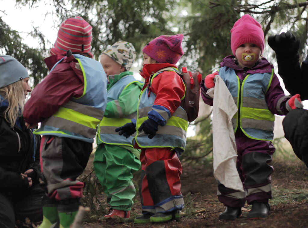 Barn med ryggsäckar och reflexvästar på sig är på skogsutflykt.